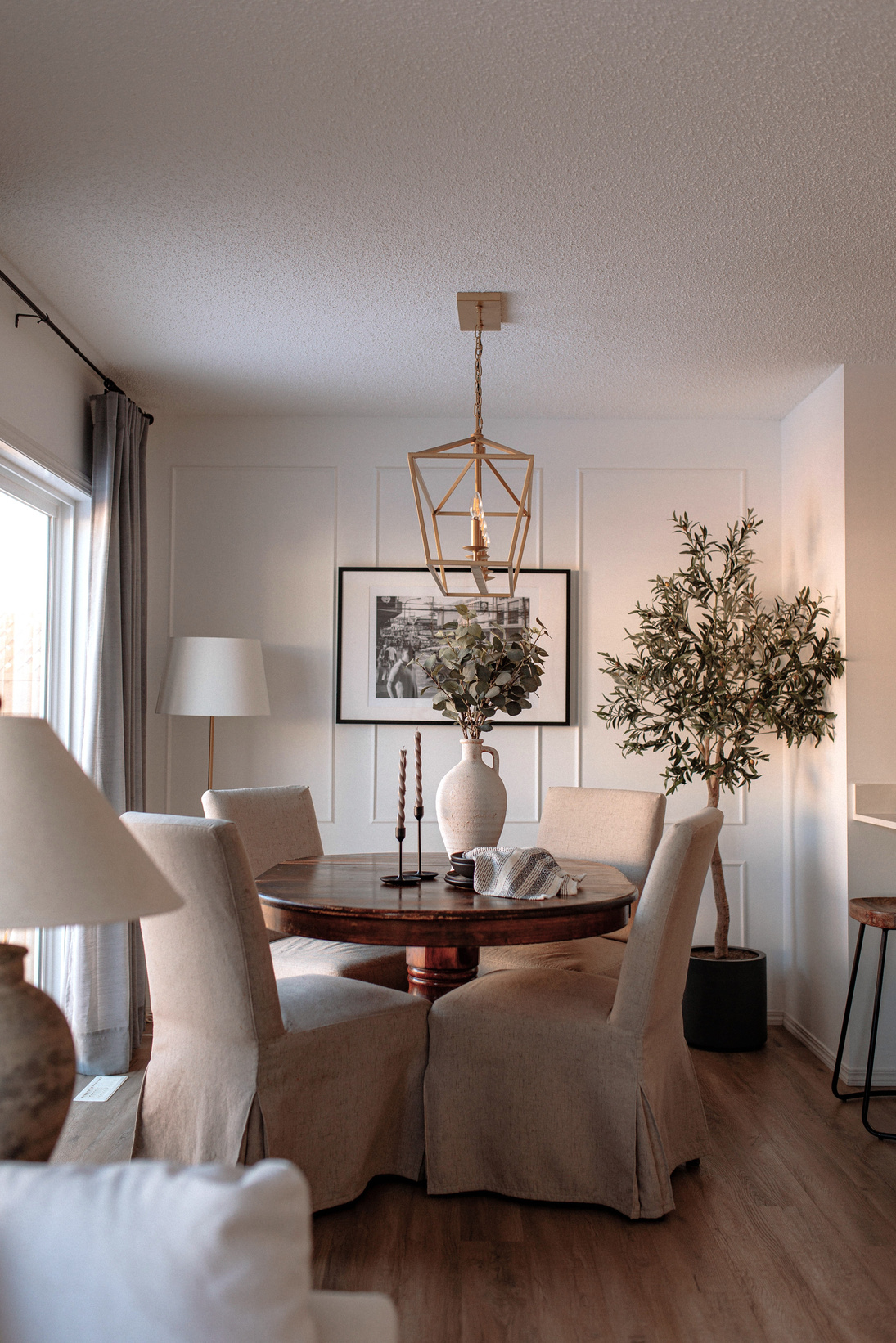 a cozy dining room with a table, chairs and a potted plant with gold chandelier designed by interior designer in Edmonton Alberta