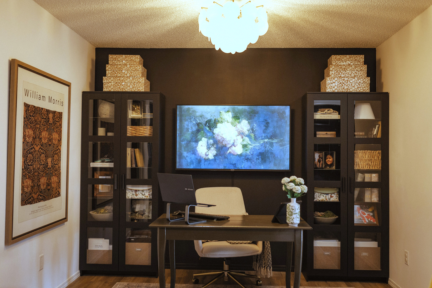 a dark moody black home office with a large flat screen tv on the wall ikea cabinets desk chair chandelier 